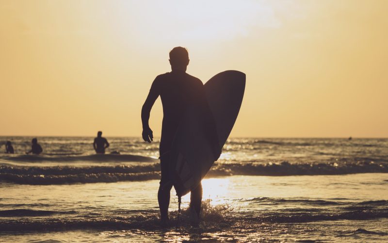 surfer-carrying-board-out-sea-sunset-time (1)